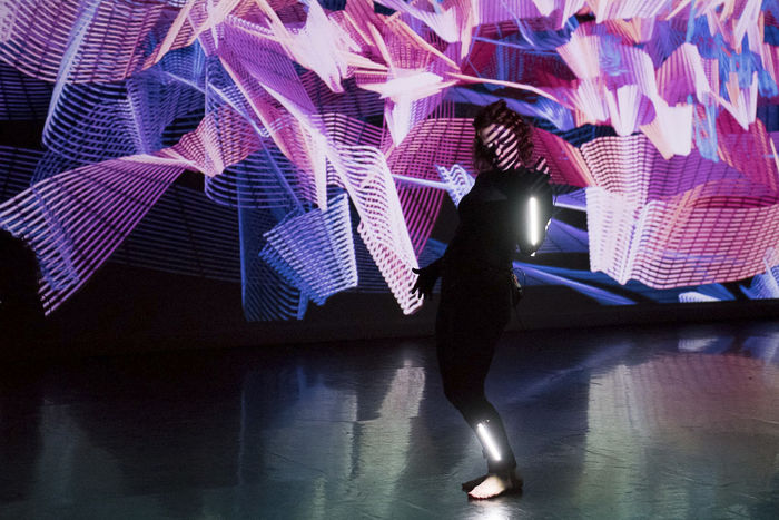 A woman performs against a backdrop of light painting and real-time projection.